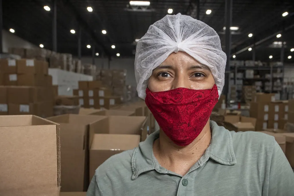 Production worker in a hairnet and face mask standing among packed cartons